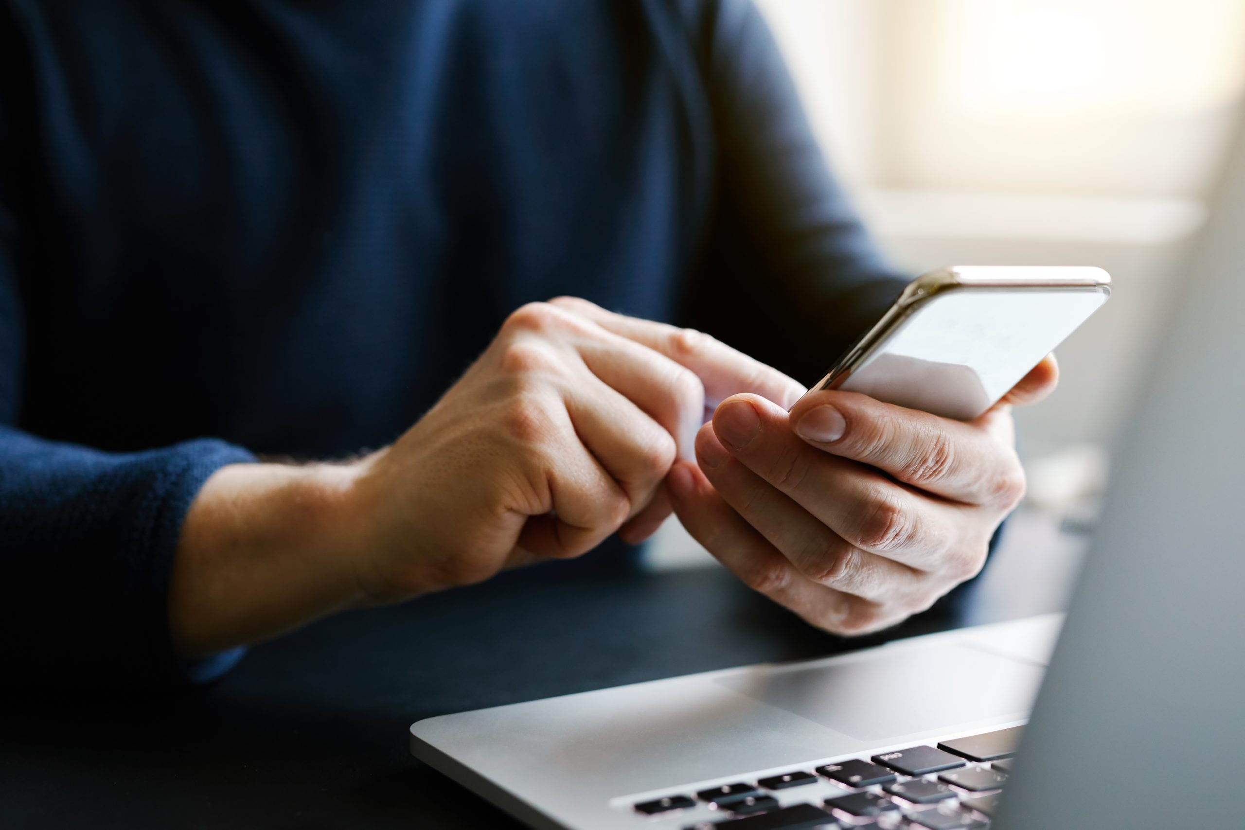 Person using mobile phone in front of laptop.